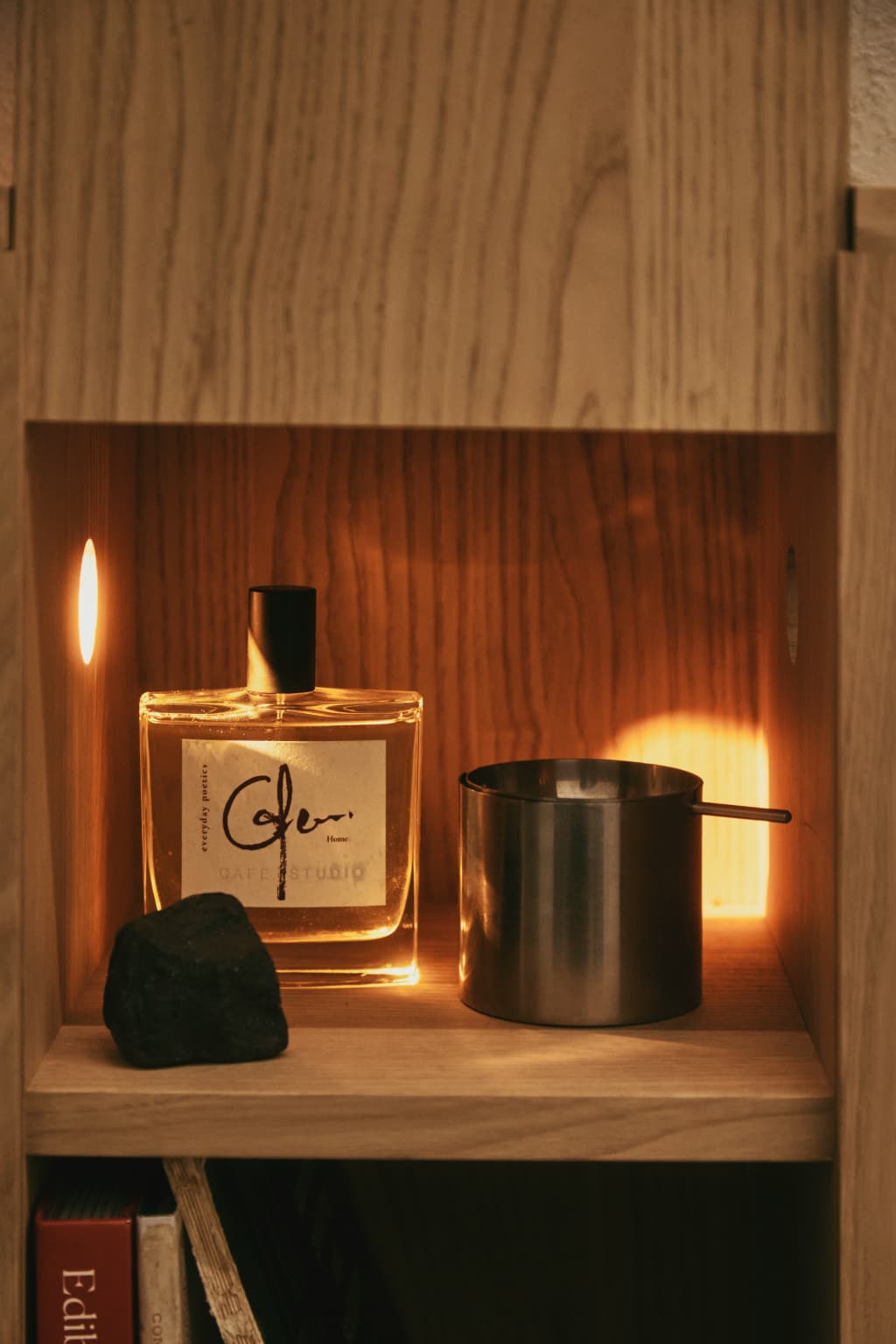 Everyday Poetics fragrance bottle and candle on a wooden shelf with warm lighting.