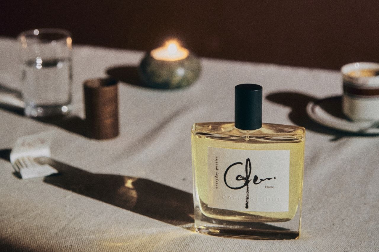 Everyday Poetics fragrance bottle on a table with a candle, and glass in the background.