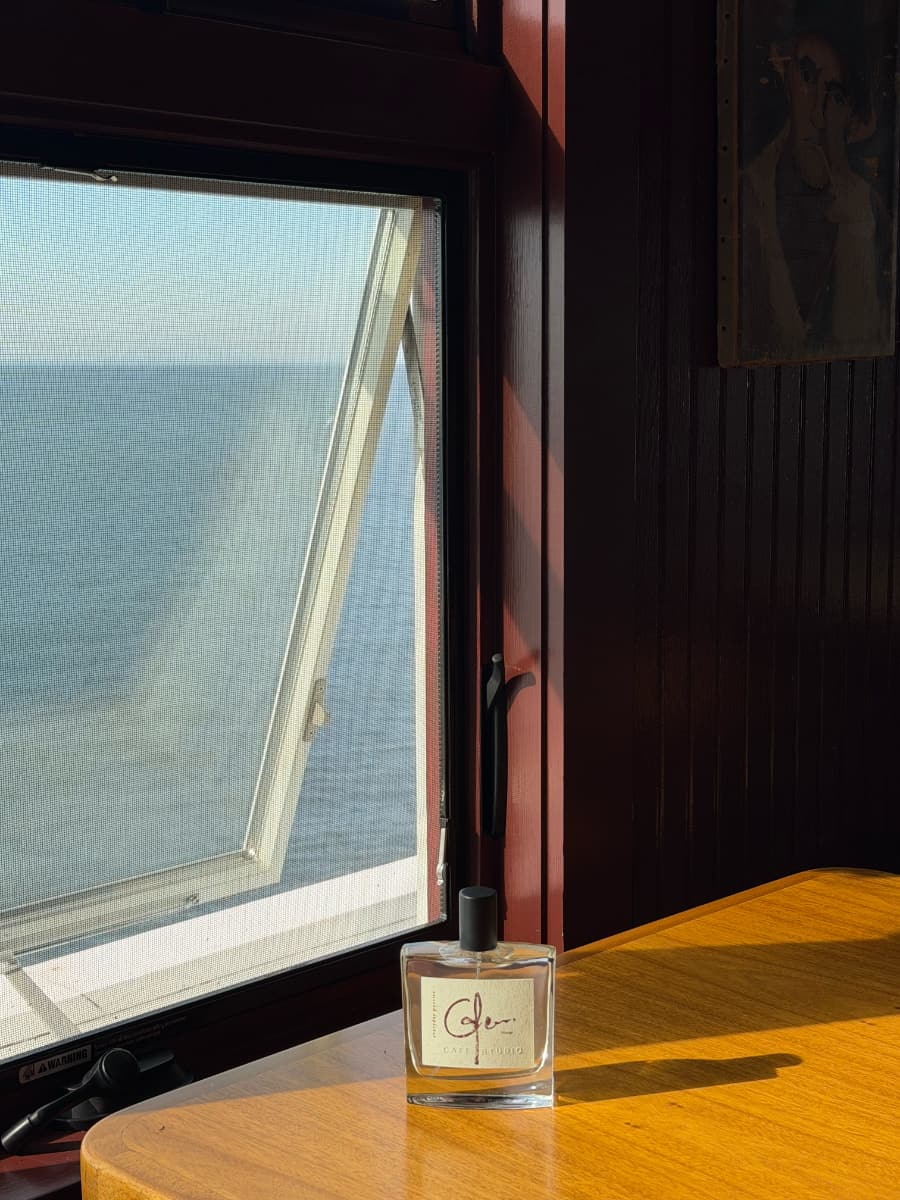 Everyday Poetics fragrance bottle by a window near the ocean.